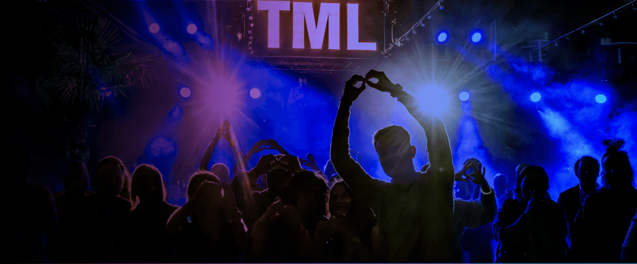 Silhouetted crowd making heart hand gestures at TML night event with blue stage lighting