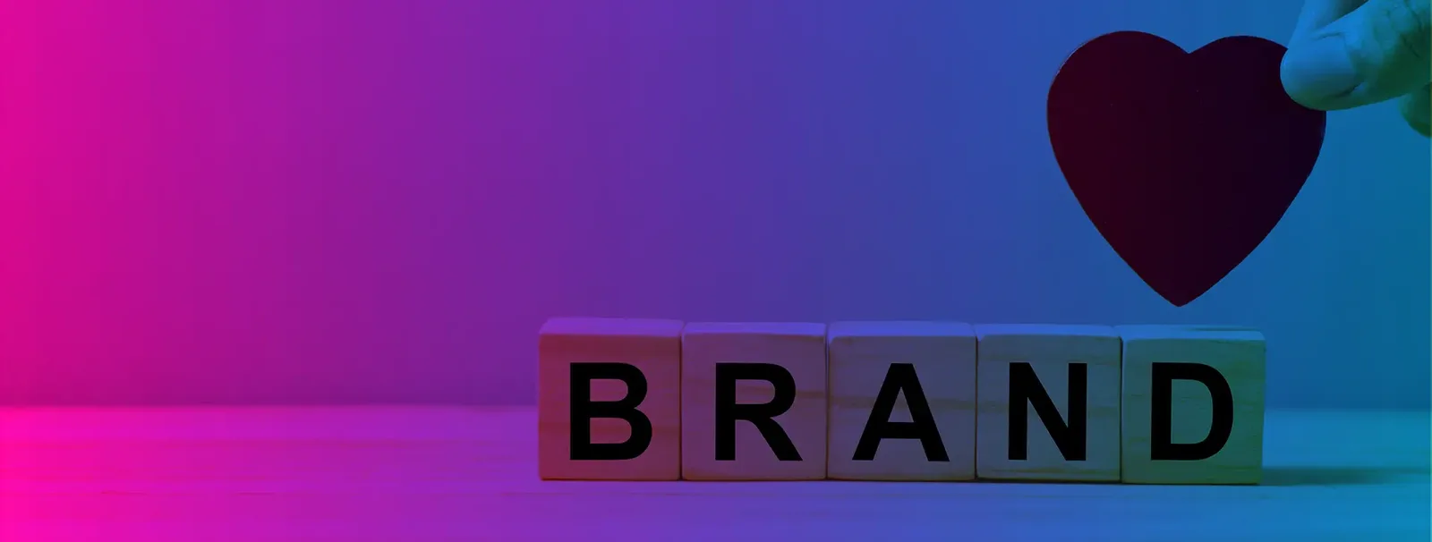 Cubes en bois formant le mot BRAND avec une main tenant un cœur au-dessus, sur fond dégradé rose et bleu